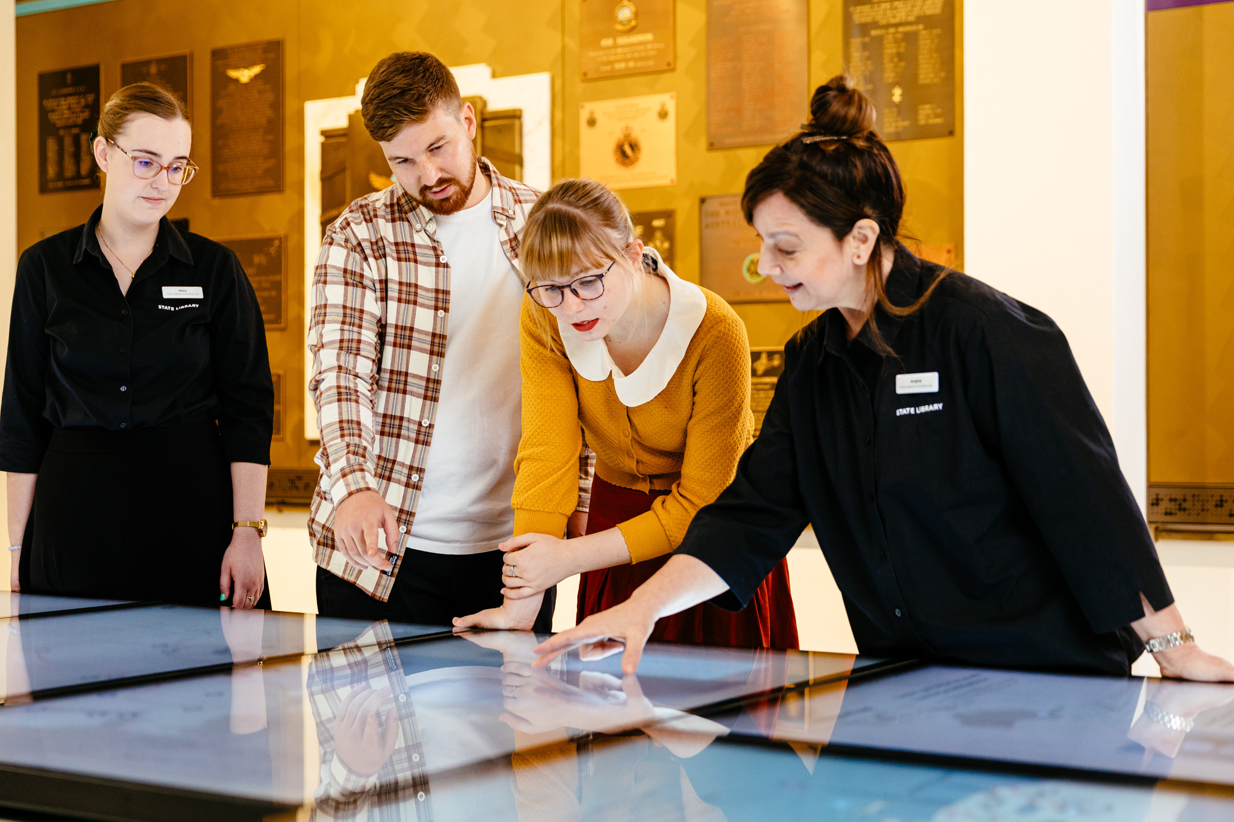 A male and female guest exploring the digital screens in the World War II Gallery at Anzac Square with guidance from staff