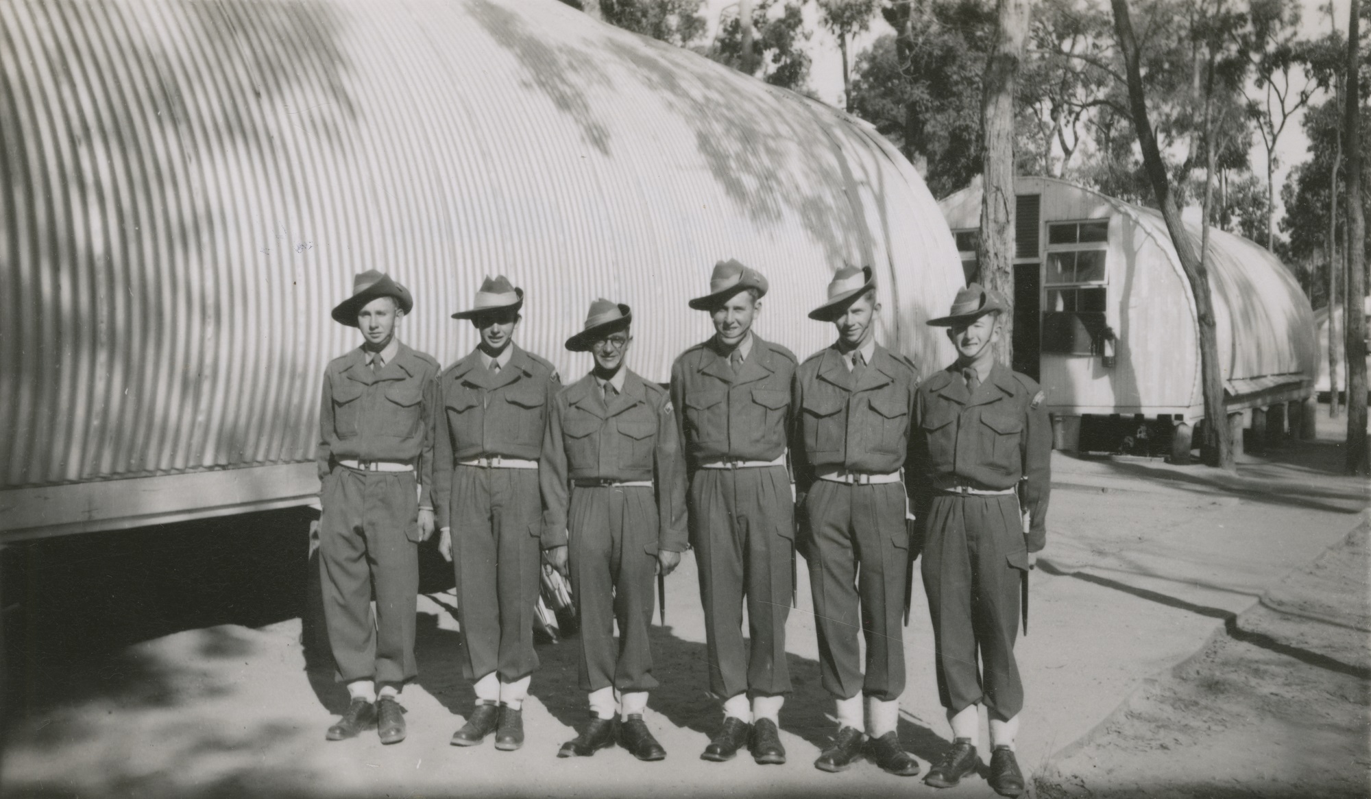 A group of soldiers standing in uniform outside a tin structure