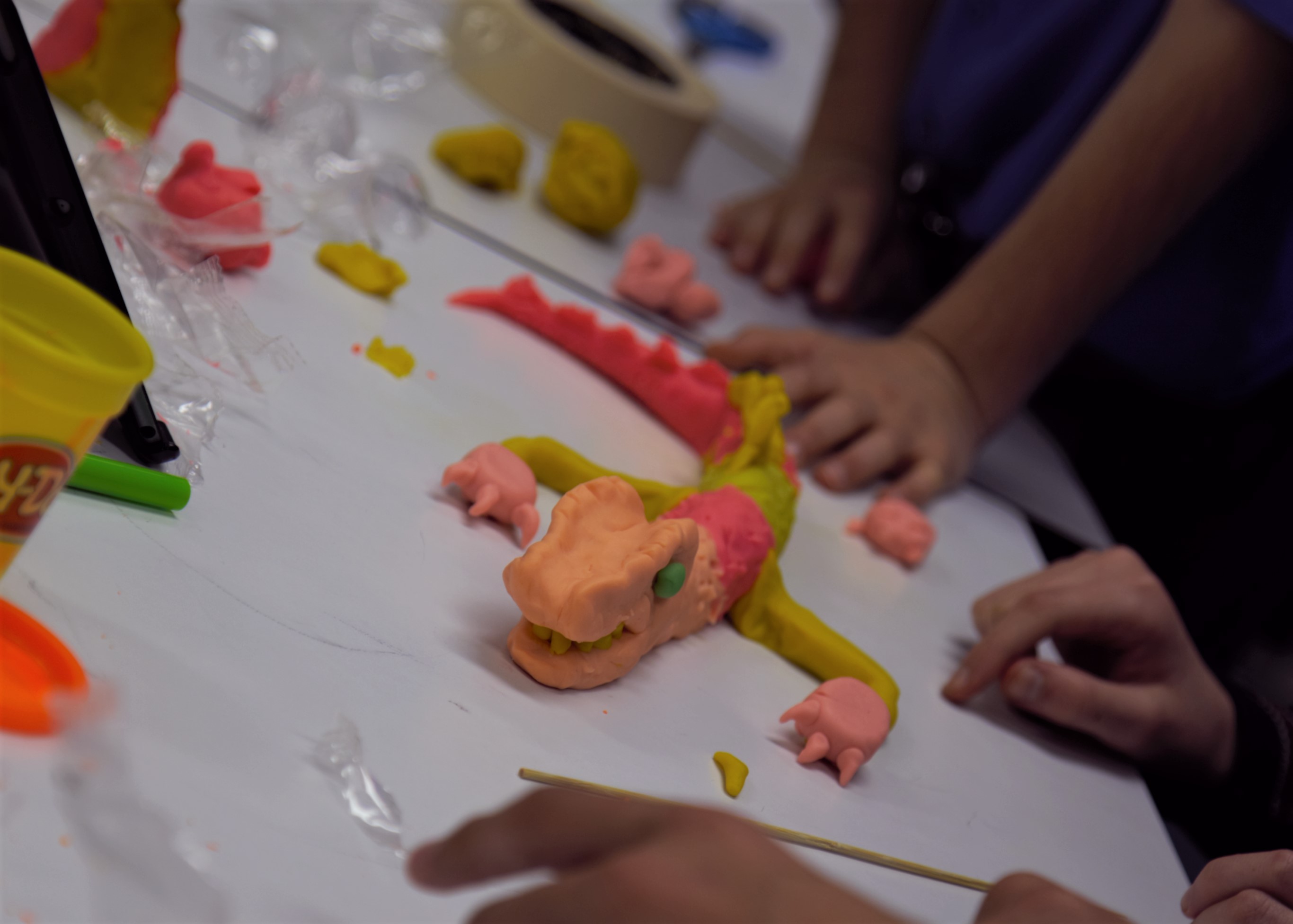 Model dragon made with plasticine and hands of children on table
