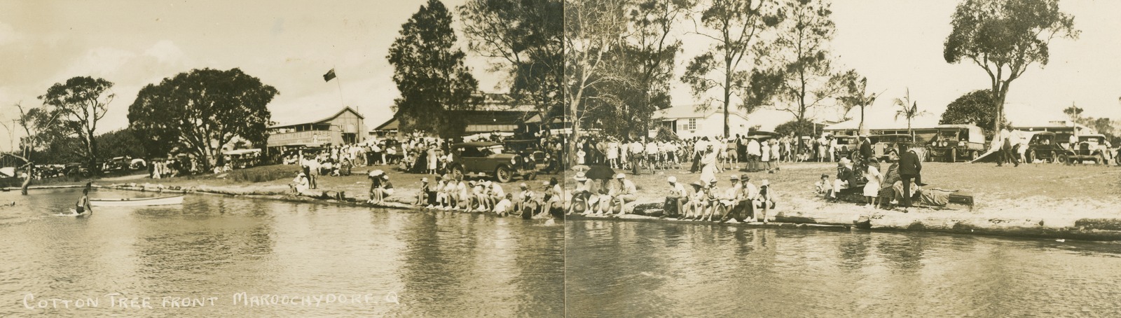 Sepia panorama image of crowds of holiday-makers gathered on the banks of the Maroochy River at Cotton Tree, Maroochydore, Queensland, ca. 1928