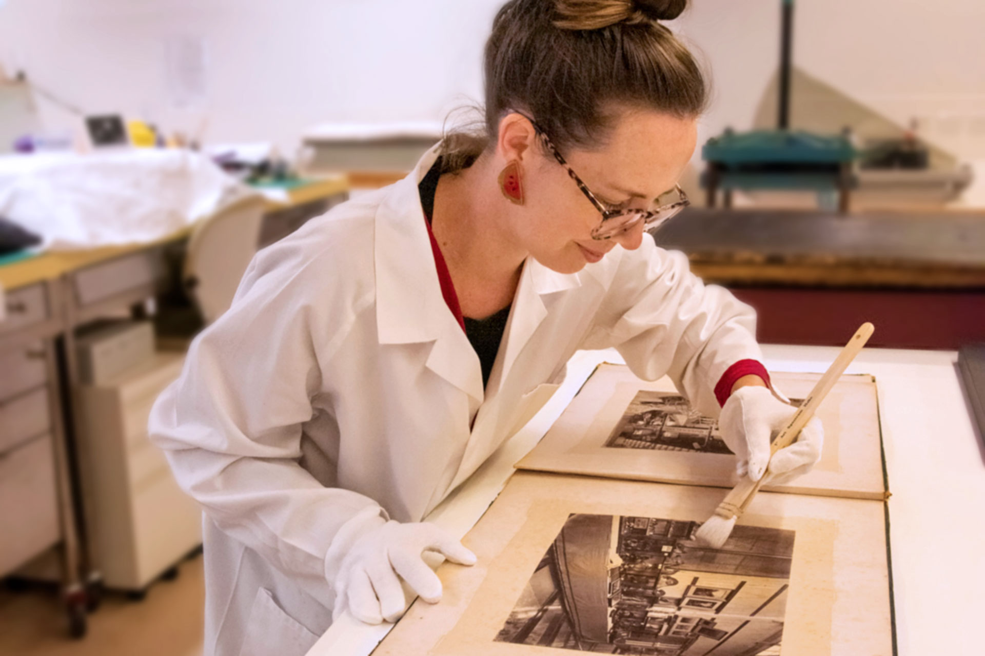 State Library staff member working in a laboratory gently brushing an old photograph.  
