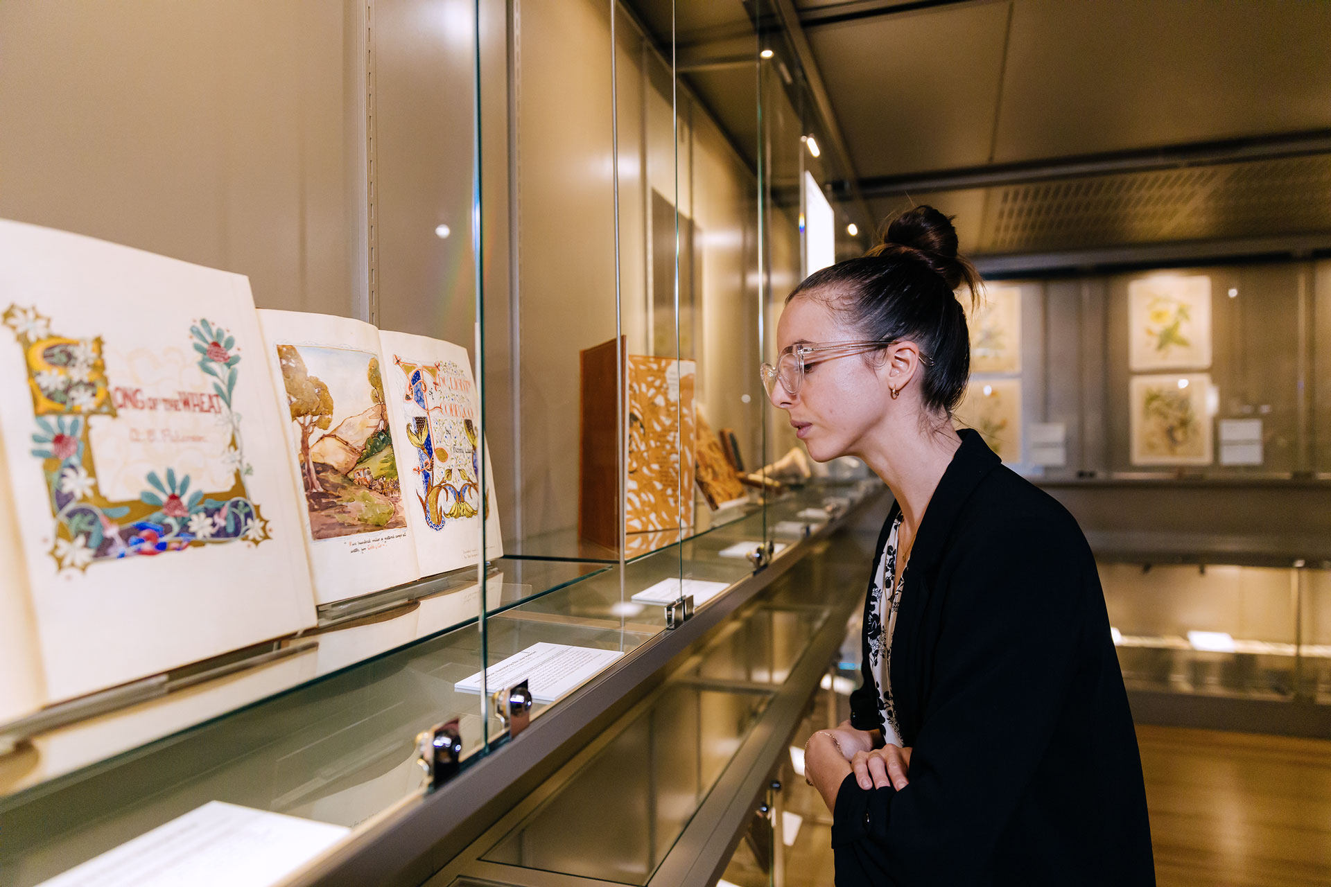 Woman looking at old illustrated book behind a glass cabinet.