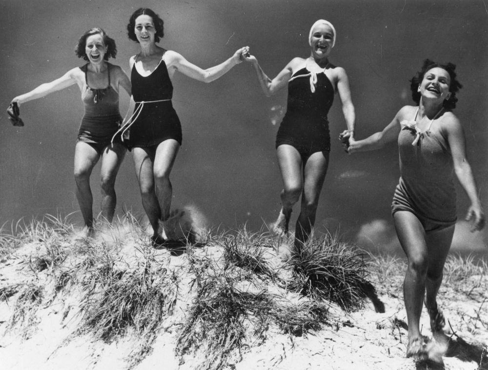 Young women running over a sand dune on an unidentified beach, ca. 1935