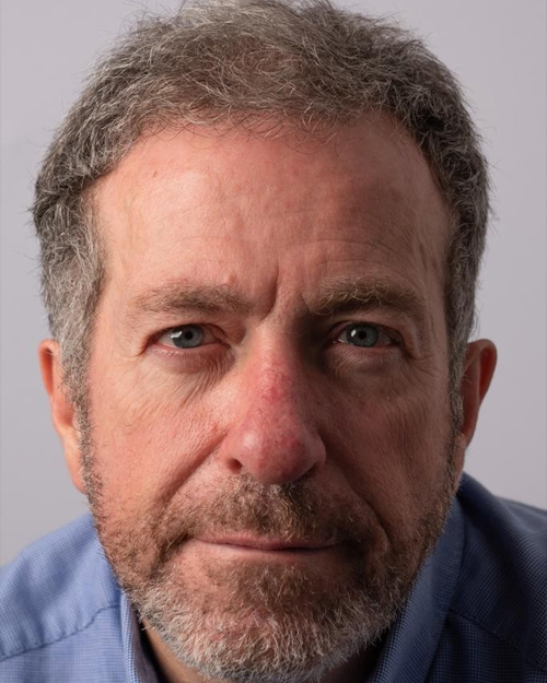 Headshot of John Richards; a close up image – John is wearing a blue button up shirt. He has a light beard and blue eyes