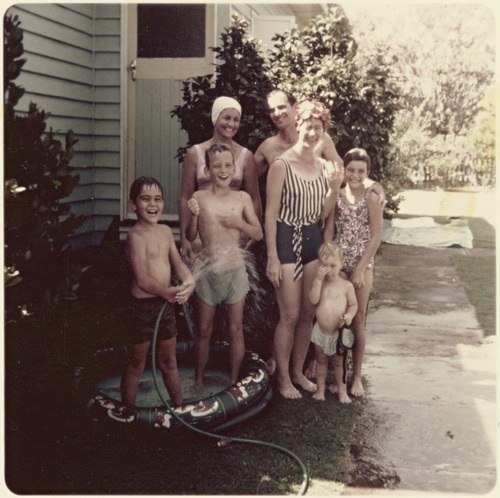 Young children and their parents play in a blow up paddle pool with a garden hose. Members of the Rolley and Croker families cooling off on Christmas Day in Beaudesert, Queensland, 1972.