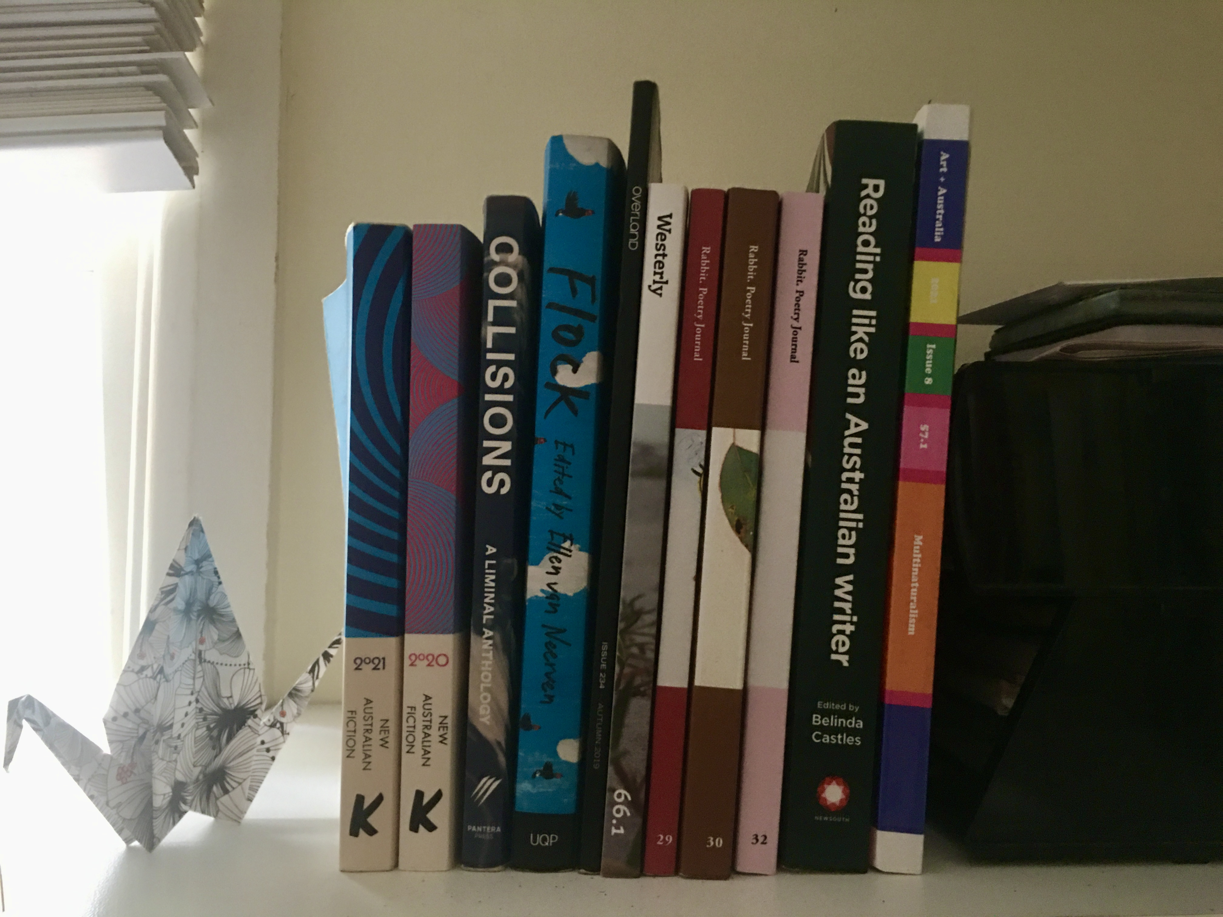 Mykaela Saunders' bookshelf including literary journals, books of essays and short story collections. A paper crane sits next to the first book.