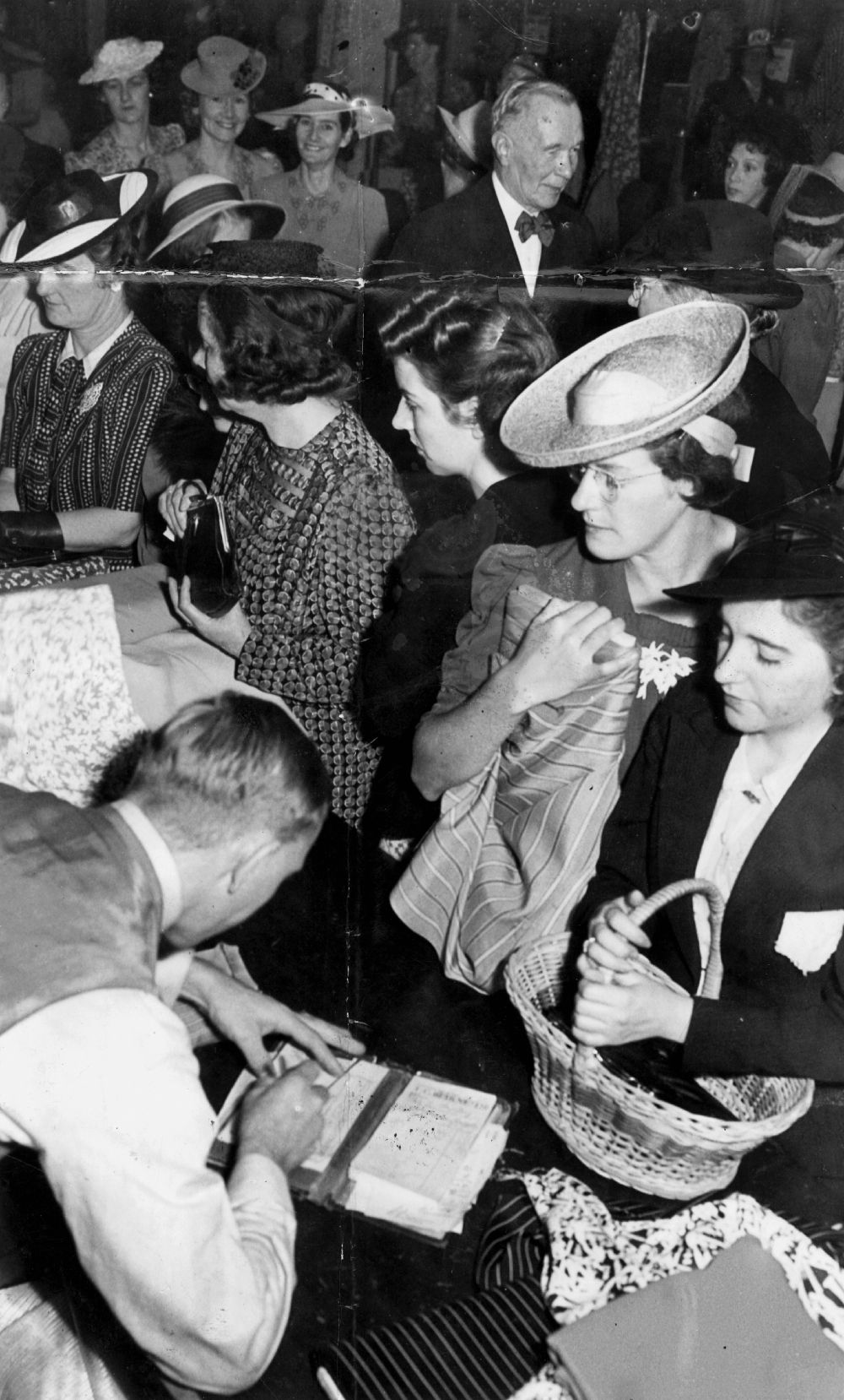 A group of women at a shop counter with a man serving them and writing in a receipt book