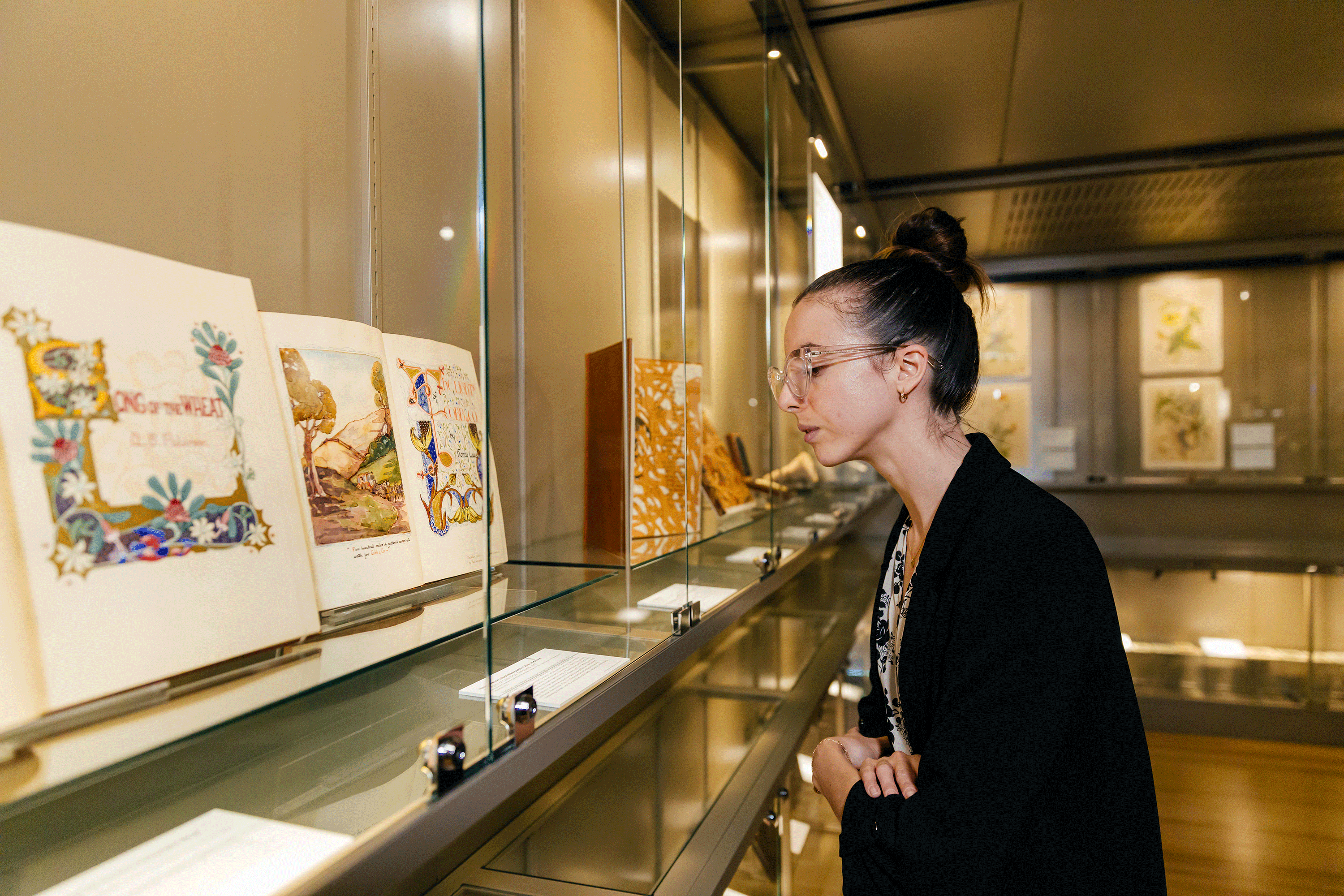 A woman looks down into a glass cabinet to inspect a display of historical books.