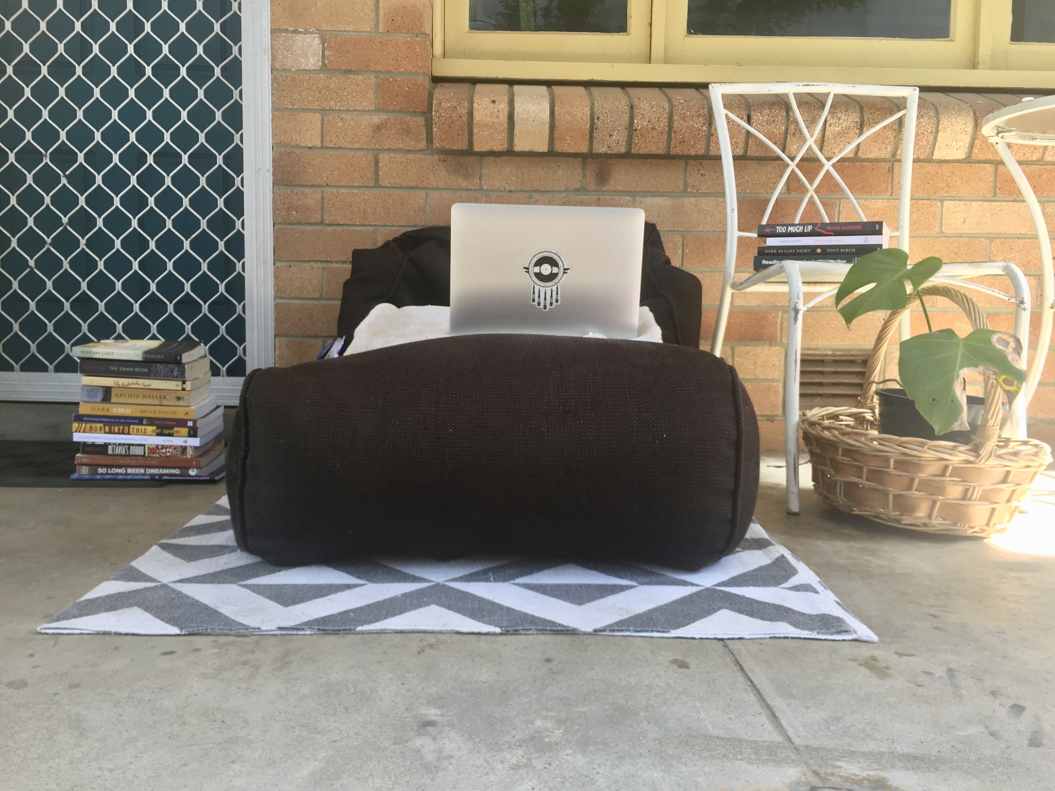Mykaela's laptop is propped up on a black beanbag outside. Next to this are chairs with stacks of books and a pot plant.