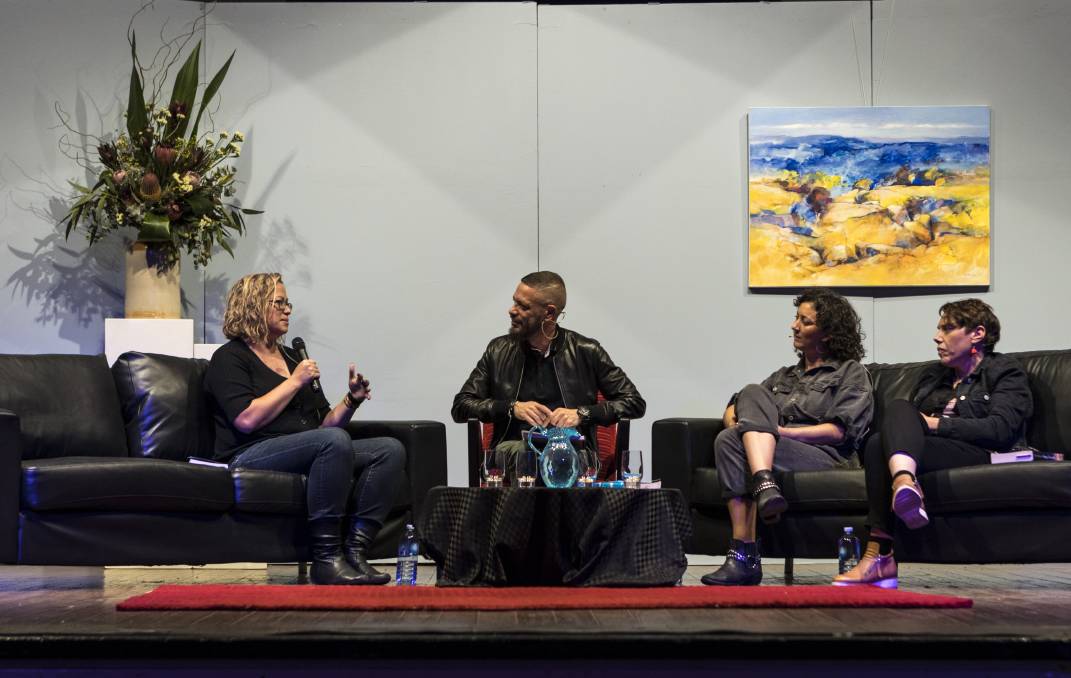 A view of a theatre stage, mid-writers festival panel with a painting and flowers in the background. Lisa Fuller, Daniel Browning, Mykaela Saunders and Nardi Simpson sit on couches. 