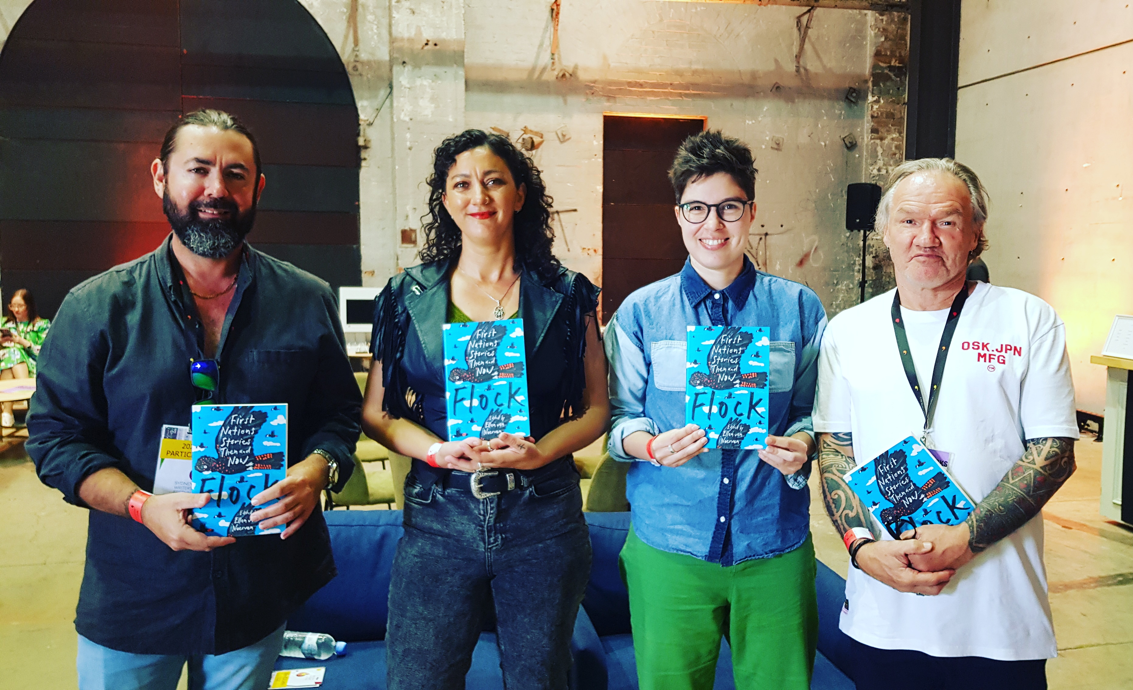 Adam Thompson, Mykaela Saunders, Ellen van Neerven and Tony Birch stand in front of a couch smiling and holding copies of the anthology, Flock