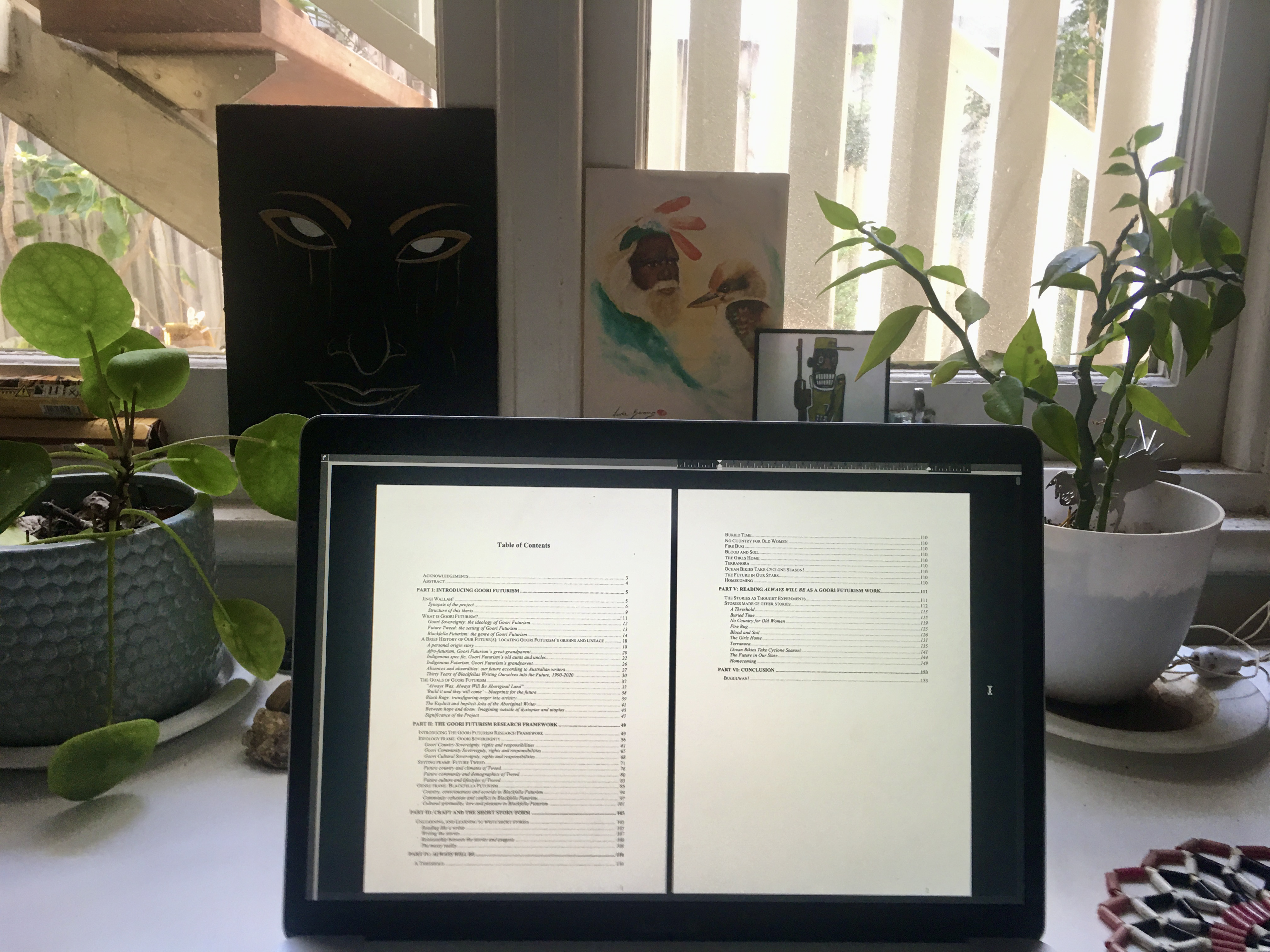 On a desk with pot plants and artwork is an iPad showing the contents page of Mykaela Saunders' PhD thesis