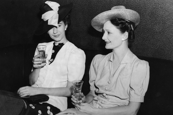 Two women enjoying a drink wearing fancy hats