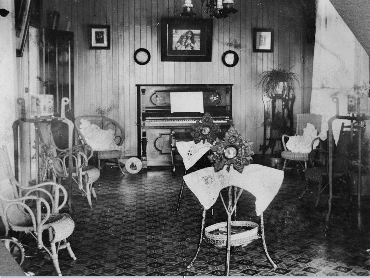 V1-FL56351 Cane furniture and a piano decorate this parlour, ca. 1915