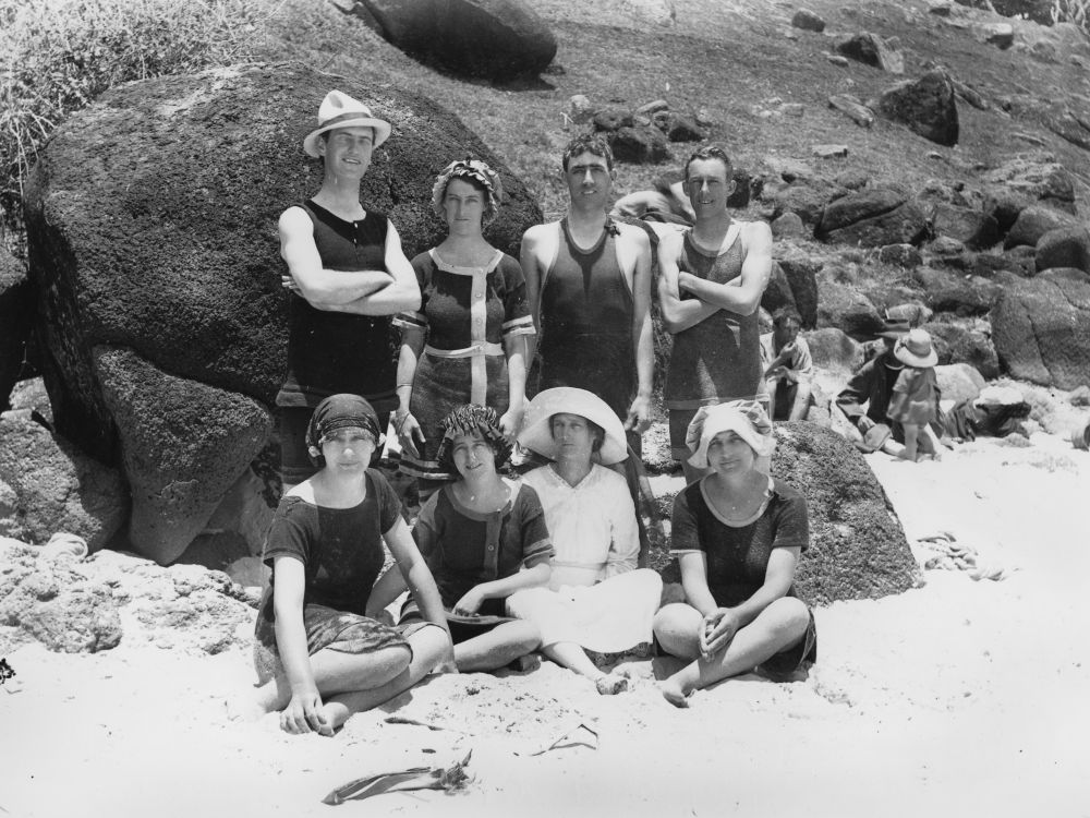 Bathers posing on a beach in hats and bonnets and modest bathing costumes typical of the early century. 