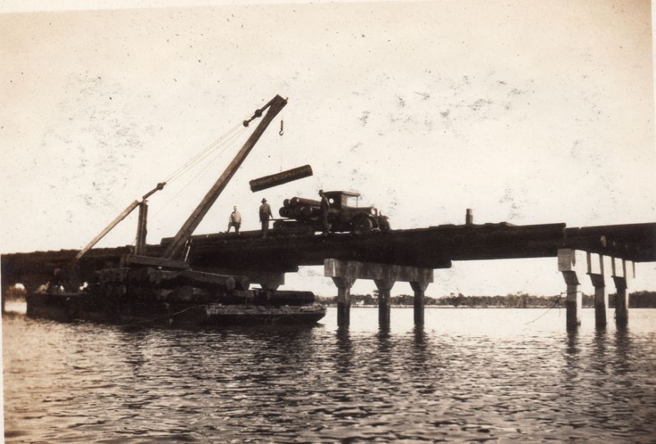 Girder supplies being loaded from a barge to be placed between the spans on the Bridge. 1752 girders were used, all 30’ lengths. They were shipped down river by barge, after coming by rail from the mills at Conondale or Mapleton