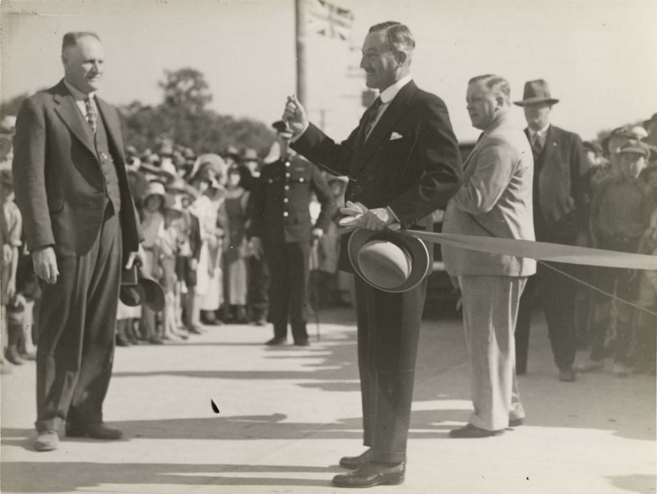 This image looks like the moment when the ribbon has been cut to open the Hornibrook Highway, by the Governor, Sir Leslie Orme Wilson. Standing opposite him is Manuel Hornibrook in a proud moment. Manuel gave the Governor a gold boomerang to mark the occasion, which was used to cut the ribbon.