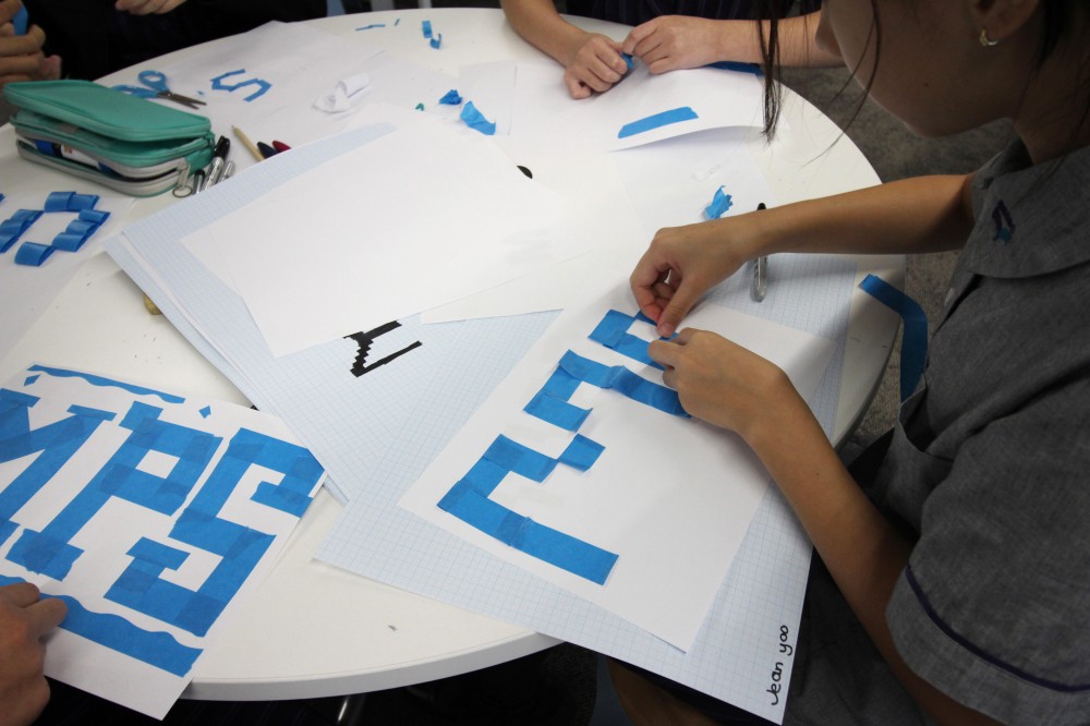 Student tearing tape to create letter shapes at a table