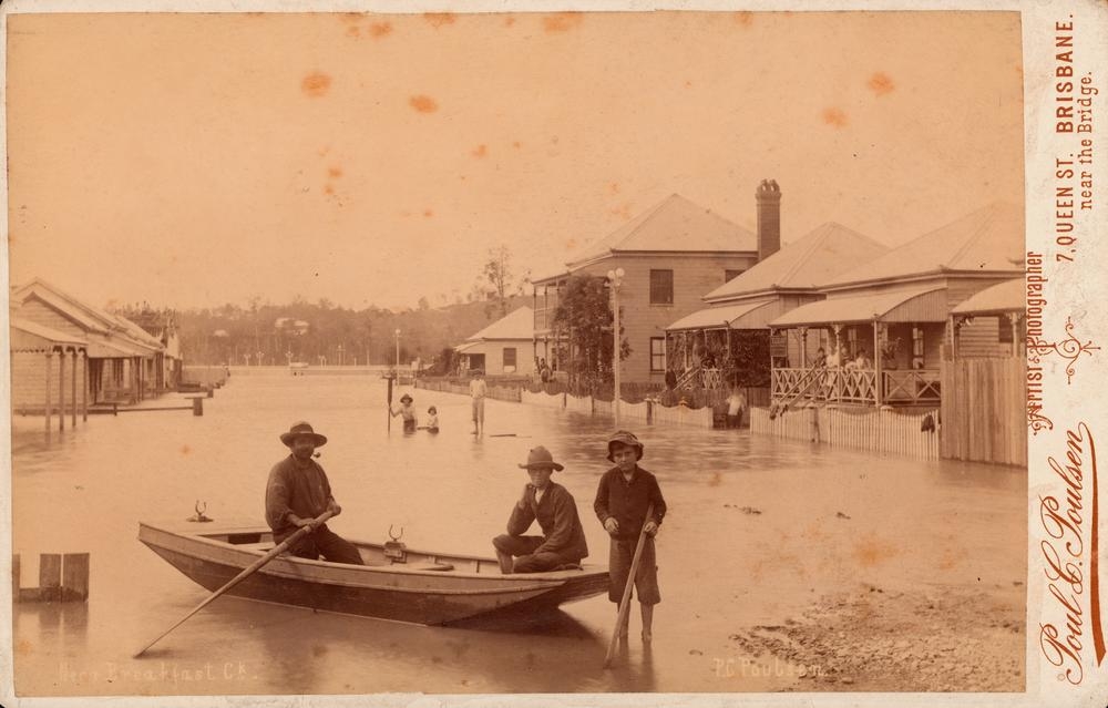 men row a boat in a flooded street 