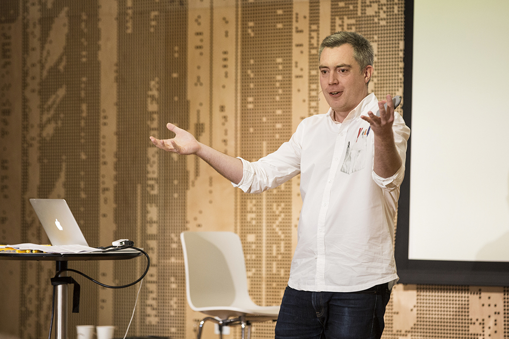 A man delivers a presentation, gesturing broadly with his hands.