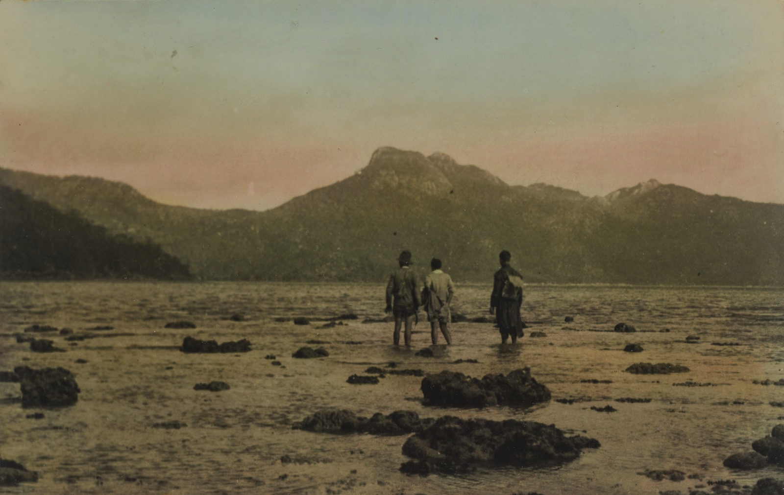 Hand coloured image of three men standing in shallow water.
