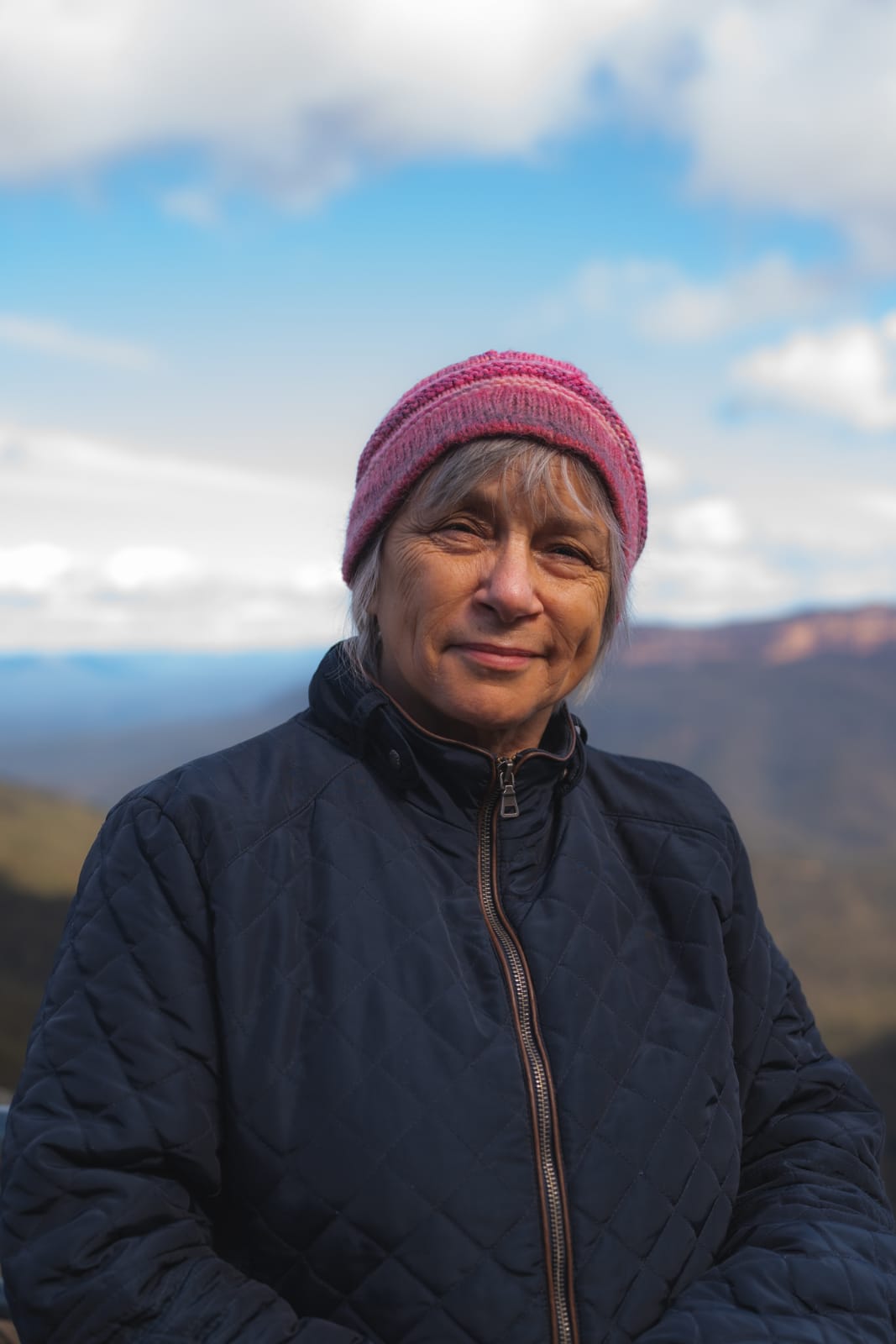 Maria van Neerven stands in a dark blue jacket and pink beanie at a mountain lookout