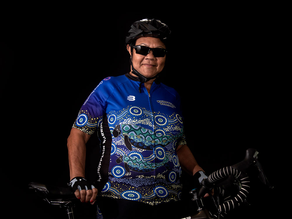 Woman wearing Indigenous sporting shirt and holding a bike