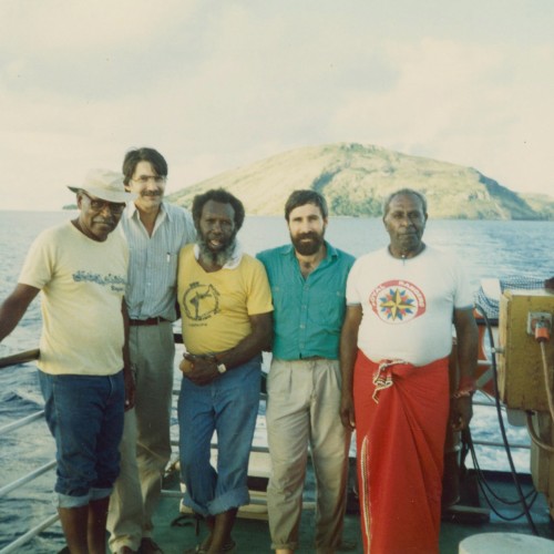 Colour photograph of five people standing on a ship at sea.