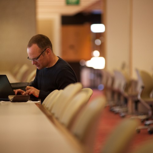 Man using a laptop near the information collections at State Library.