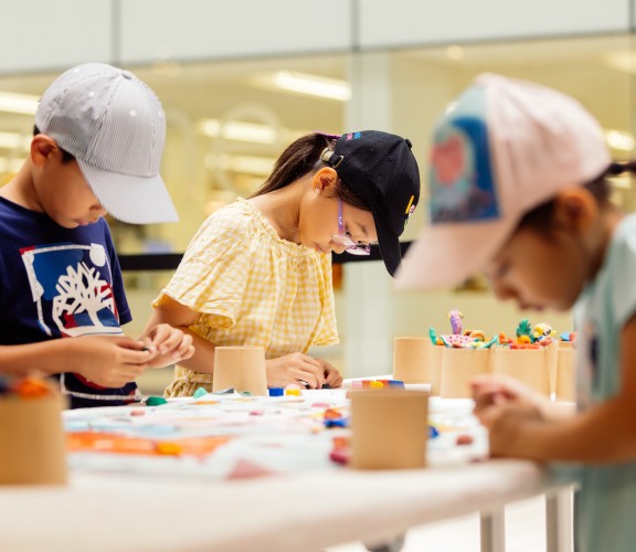 Three children crafting at a table using colourful clay.