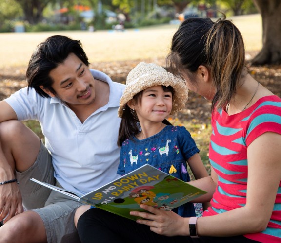 Father and mother reading book with daughter in park