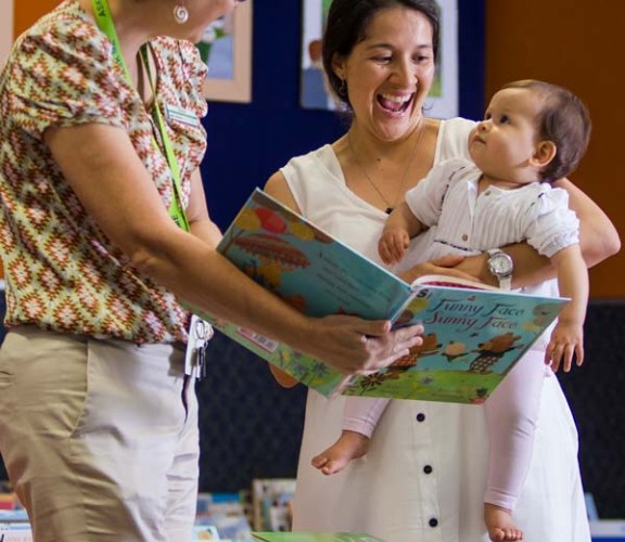 Woman and baby reading book with librarian