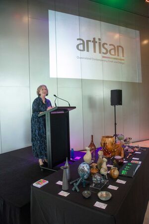 woman in blackand blue flowered dress speaks at podium with artisan logo projection in background