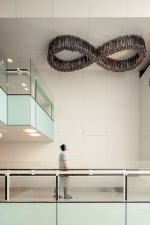 A man walks beneath Black Opium by Fiona Foley, an art installation on a white ceiling