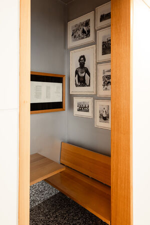A view of a room that is part of "Black Opium" by Fiona Foley, showing black and white photos of Aboriginal people framed on the wall