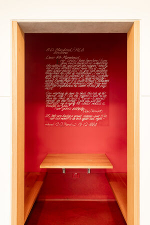 View of a room that is part of "Black Opium" by Fiona Foley; the room is red and includes a large print of a hand-written letter from 1884