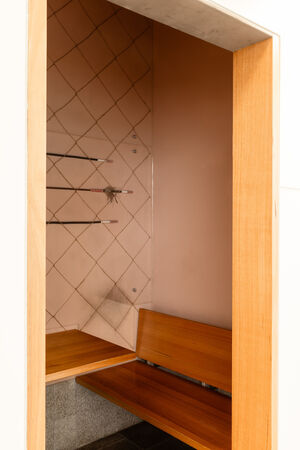 View of a room that is part of "Black Opium" by Fiona Foley; the room contains a wooden seat and 3 spears on the wall