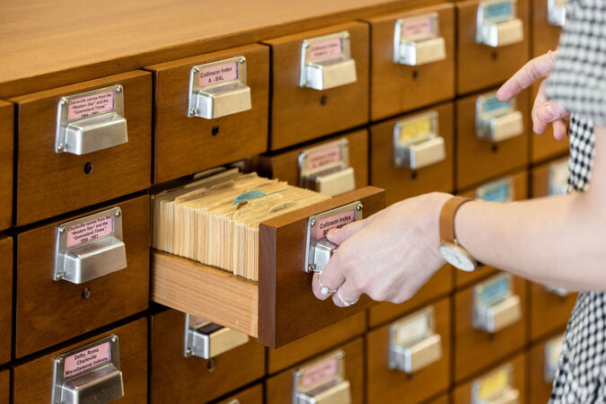 Close up of a person opening a vintage card catalogue in a library