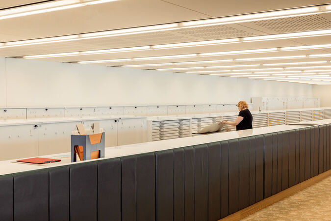 Interior of a library showing long white benches, drawers for maps and a person sorting through paper