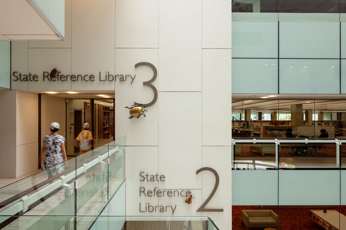 Two people walk into the state reference library; Christmas beetle artwork is on the wall