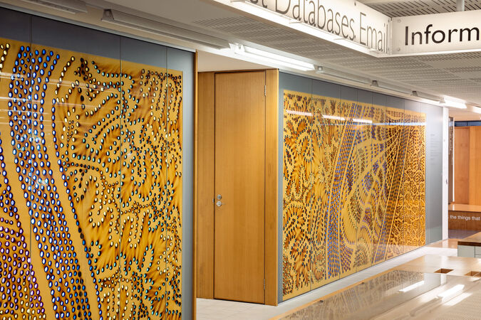 Interior view of a library information desk with an artwork behind it that shows bright spots on burnt brown paper