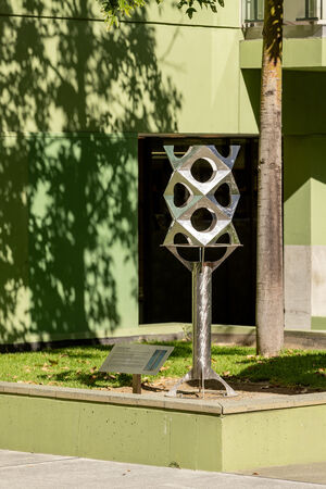 Front entrance of State Library of Queensland showing green balconies and a tree casting a shadow and the 'Paradigm' maquette by Jon Barlow Hudson