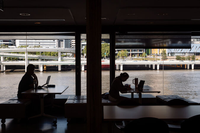 Two people in silhouette working at desks; through the glass behind them is a view of the river
