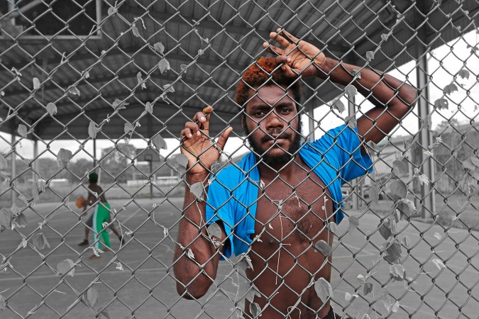 Aboriginal man in a blue shirt behind the fence of a outdoor basketball court