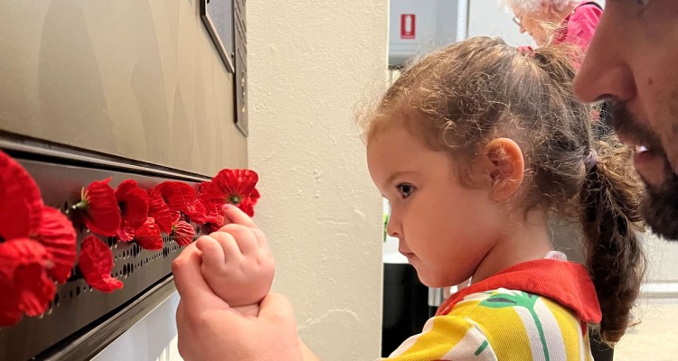 Little girl putting poppy on wall at Anzac Square