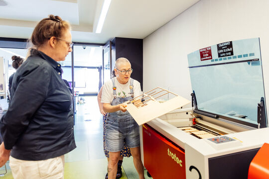 The Edge patrons inspect a laser cut sheet of plywood in front of the laser cutter at The Edge.