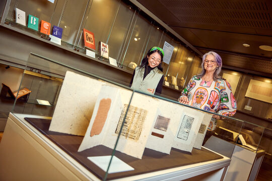 Two people standing behind a glass display case in the Australian Library of Art Showcase at State Library of Queensland. 