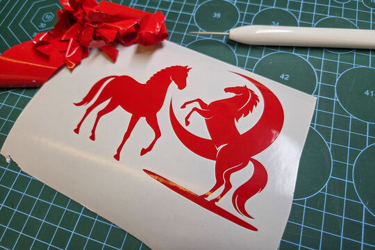 A sheet of two red vinyl stickers in the shapes of horses. They have been recently weeded.