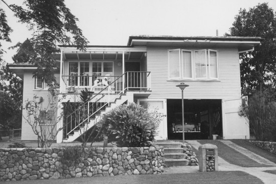 A black and white photograph of a double story house with a stone wall