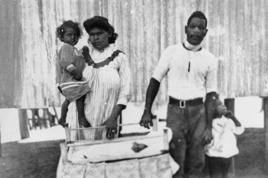 Two Aboriginal parents and their two children standing behind a baby's cot